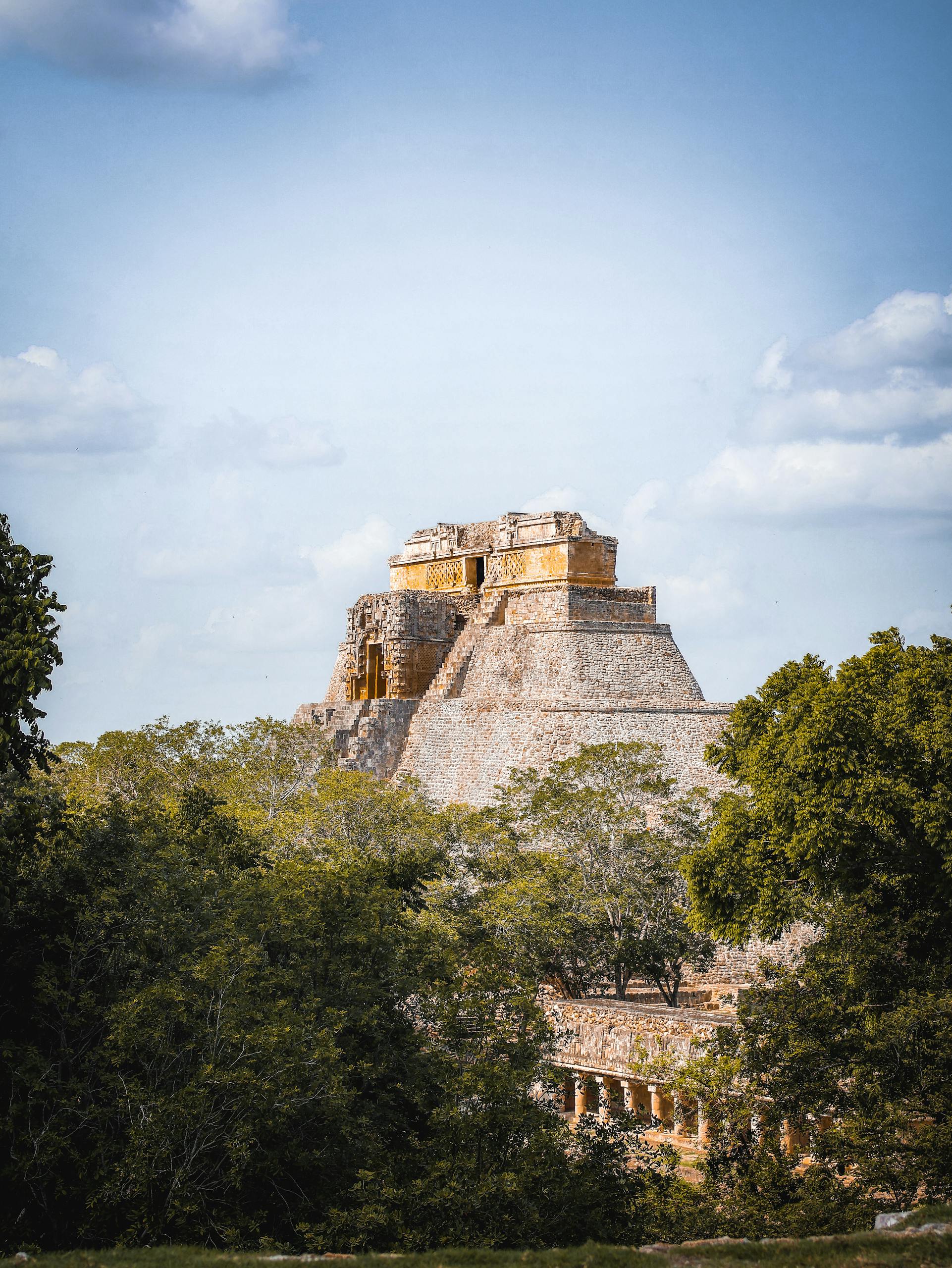 Explore the iconic Pyramid of the Magician in Uxmal, Yucatán, surrounded by lush greenery and blue sky.
