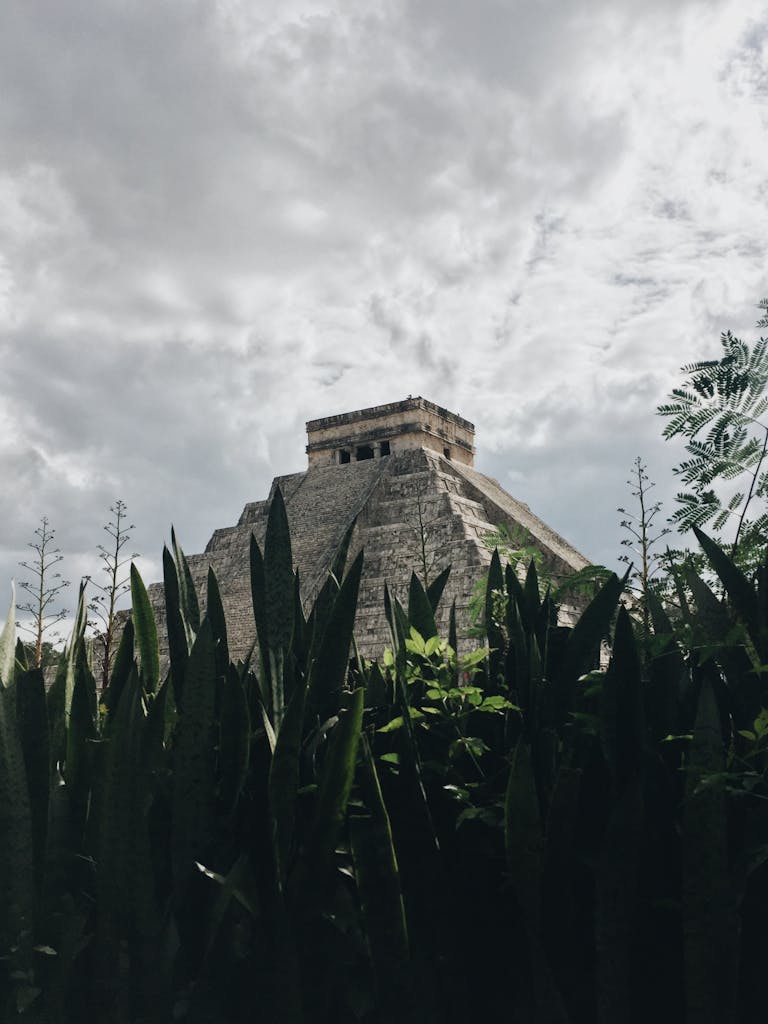 Low angle view of Chichén Itzá's El Castillo pyramid partially obscured by lush greenery.